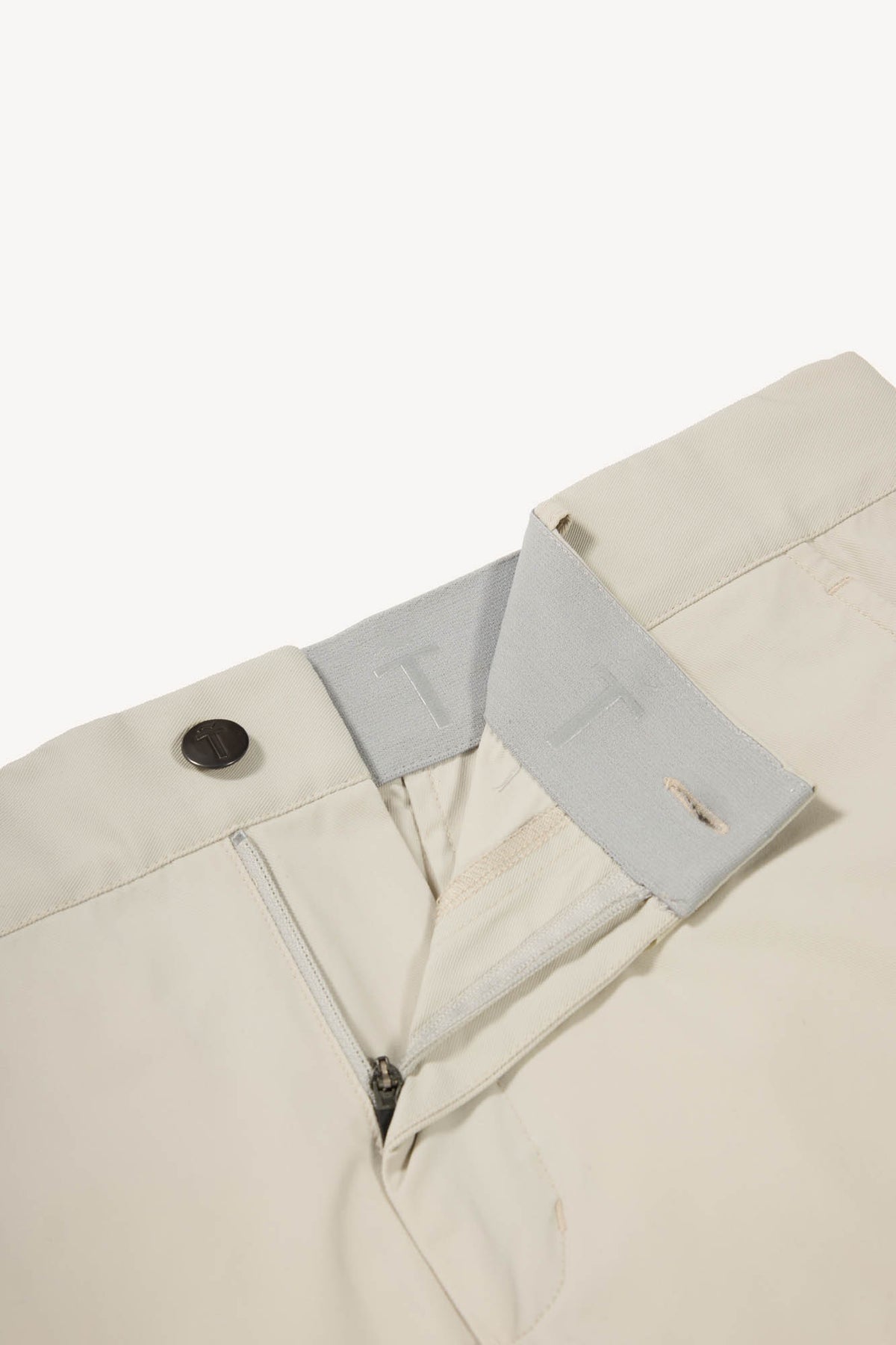 Close-up of beige pants with a light gray waistband and button on a white background