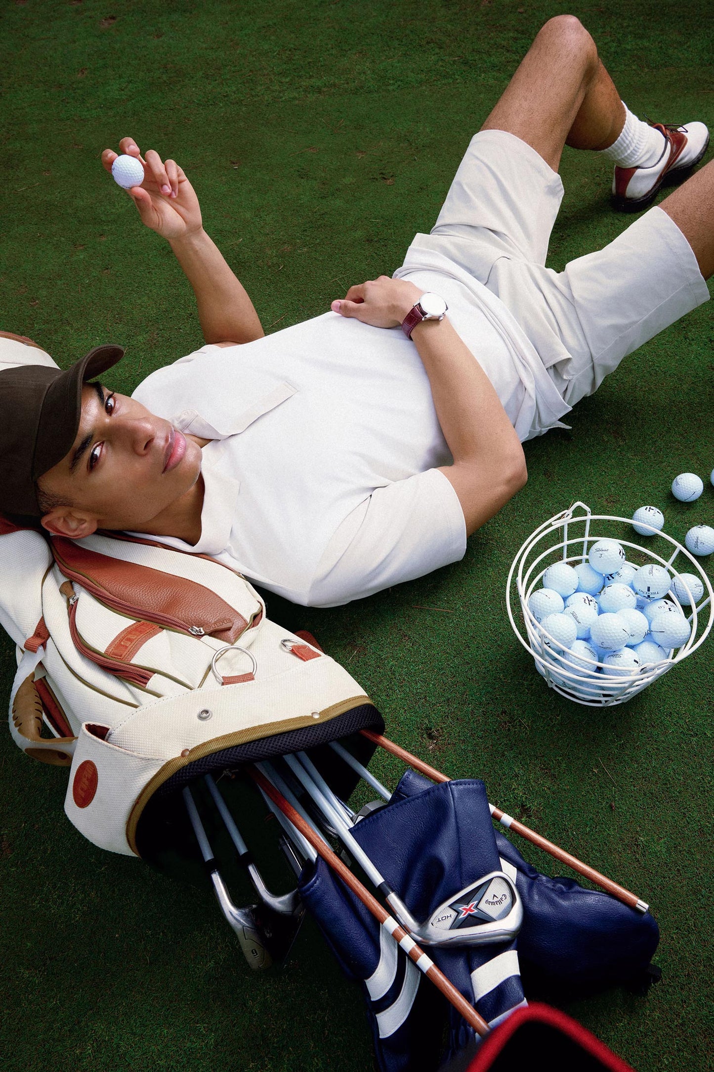 Person lying on grass with golf equipment and balls