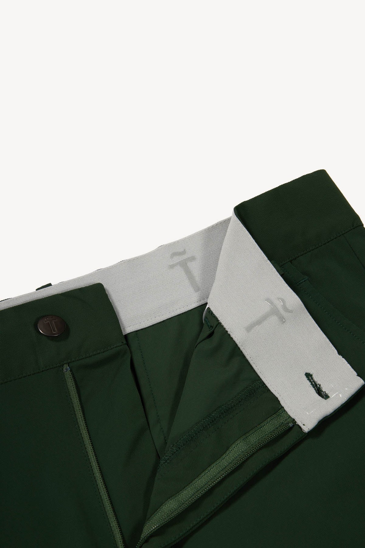 Close-up of green pants with a elastic band with silicon detailing and brand logo on a white background