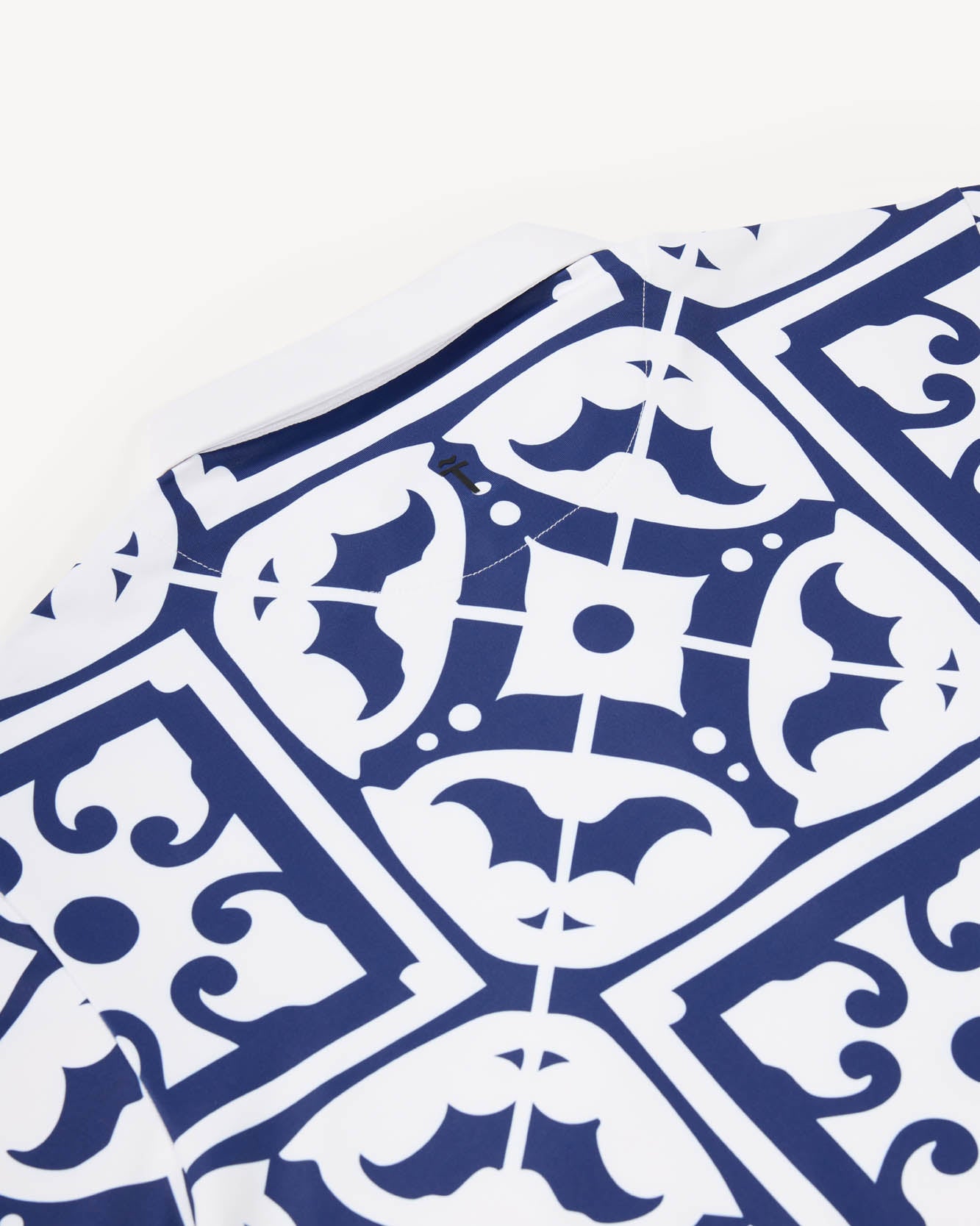 Close up of a white performance polo golf shirt with blue geometric pattern resembling tiles found on the Iberian peninsula on a white background