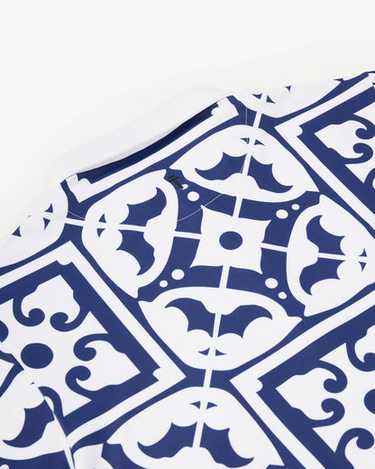 Close up of a white performance polo golf shirt with blue geometric pattern resembling tiles found on the Iberian peninsula on a white background