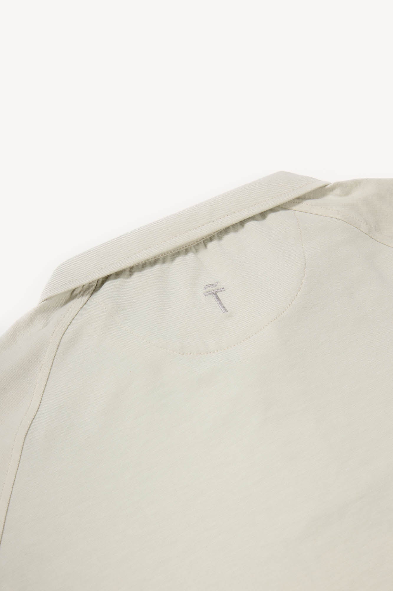 Close-up of a tan cotton polo with a brand logo on a white background