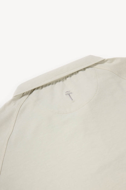 Close-up of a tan cotton polo with a brand logo on a white background
