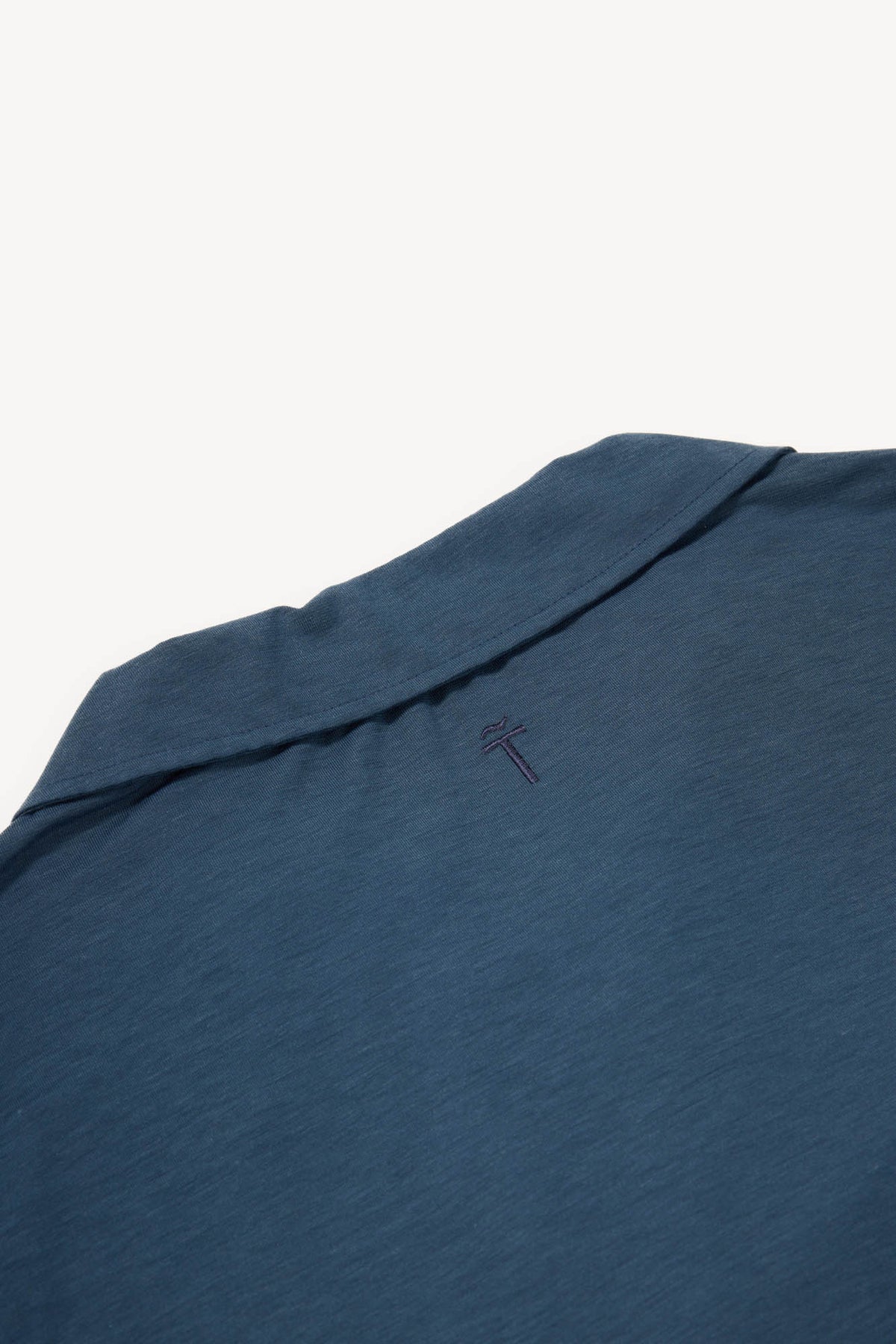 Close-up of a blue grey cashmere polo  with a subtle brand logo on a white background