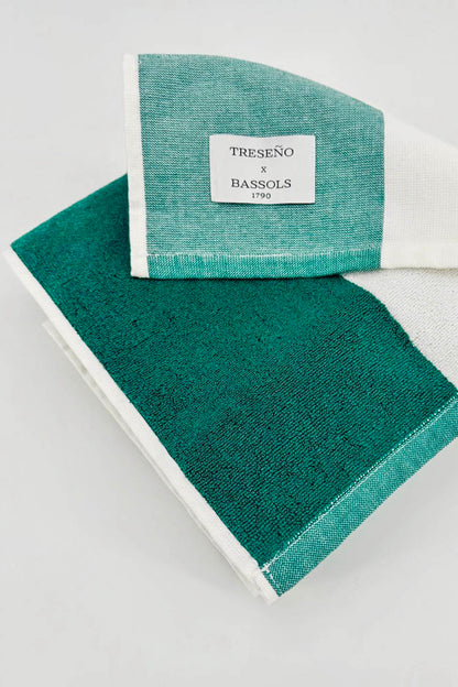A folded cotton towel with a color-blocked design in deep teal green and mint green, finished with a white border and a white brand label that reads 'TRESENO x BASSCLS (F)30'.