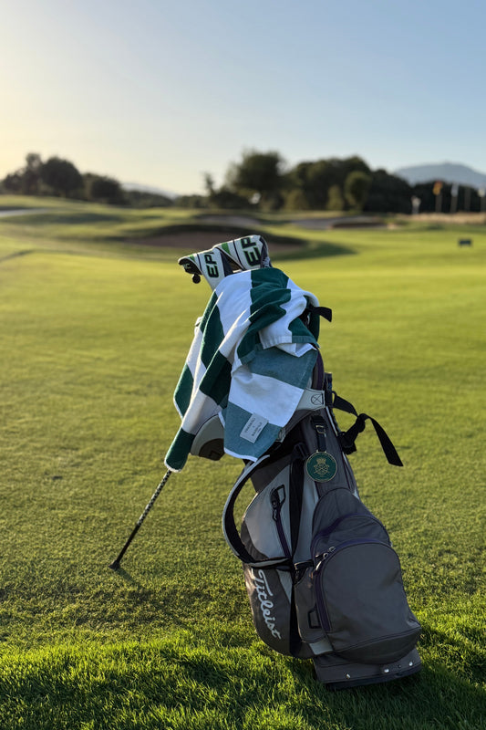 A gray and black Callaway golf bag standing on a grassy golf course, with a green and white striped golf towel draped over the top and a golf club resting in the bag.