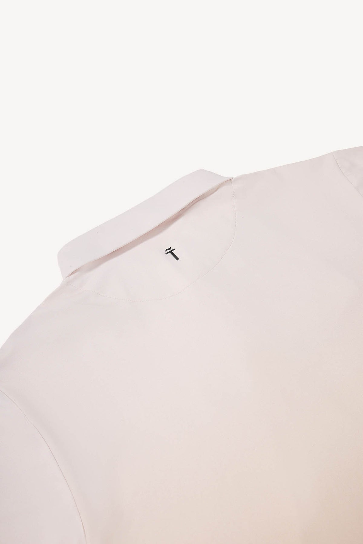 Close-up of a light tan polo shirt with a small logo on the collar against a white background