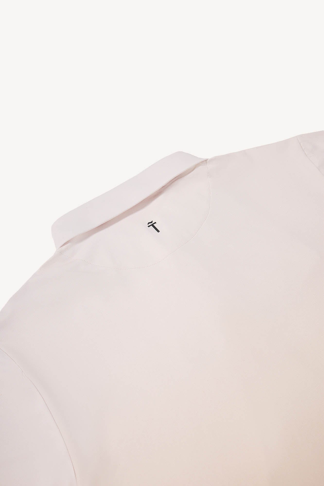 Close-up of a light tan polo shirt with a small logo on the collar against a white background