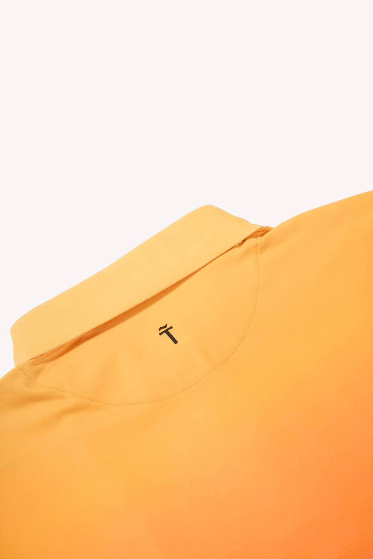 Close-up of an orange gradient performance golf polo shirt with a small ´Treseño golf logo on a white background
