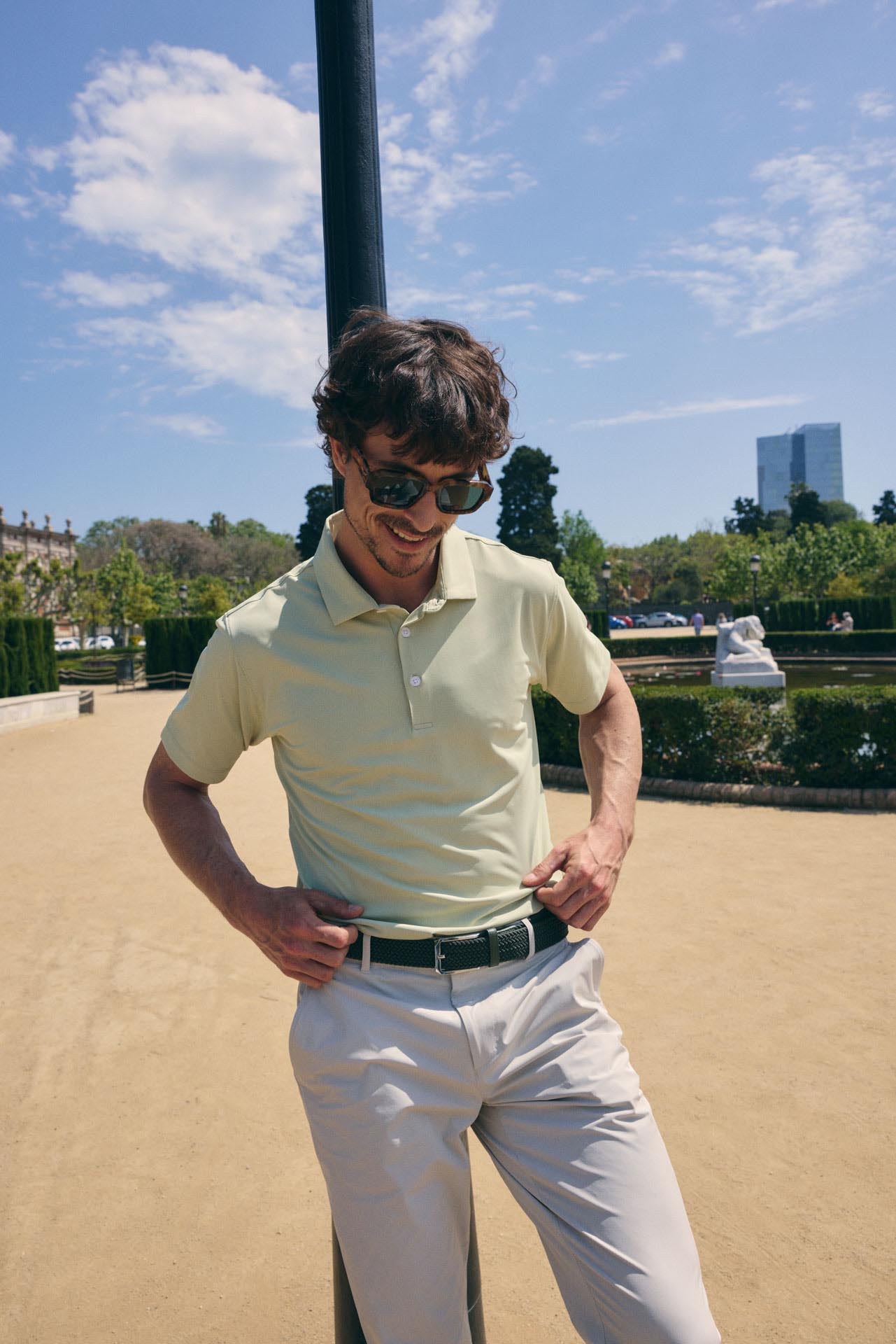 Man in a light-colored shirt and sunglasses standing outdoors with a clear sky and trees in the background.