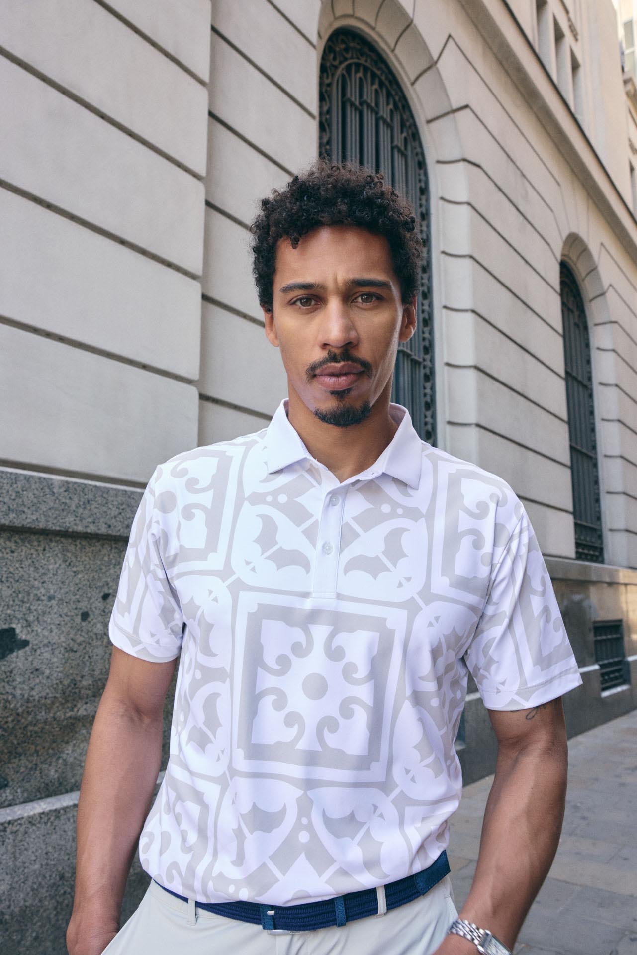 Man wearing a white patterned shirt standing in front of a building