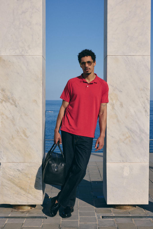 Man in a red polo shirt and black pants standing against a marble wall with ocean view