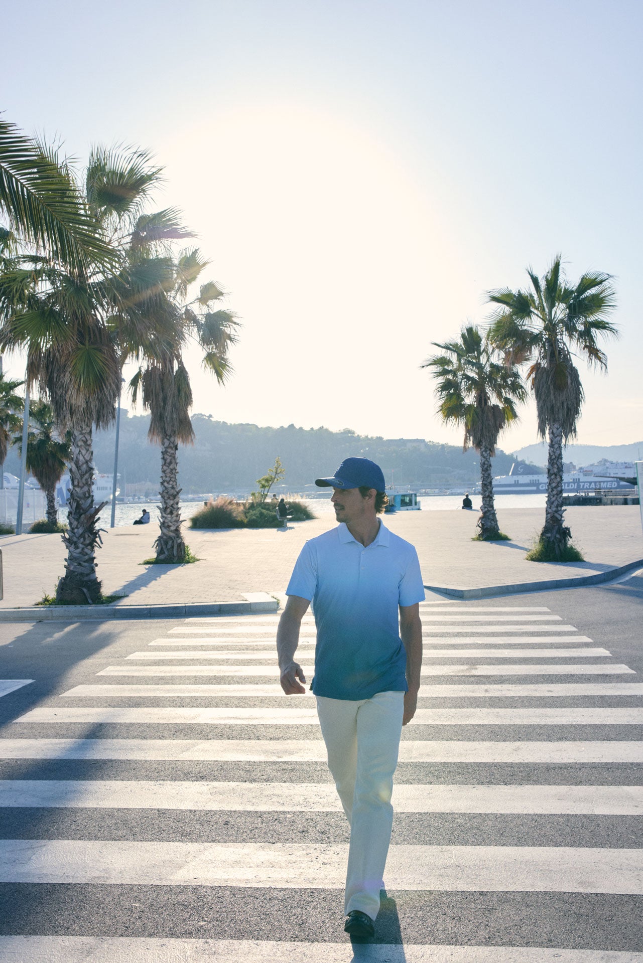 Man walking on a pedestrian crossing with palm trees and a clear sky in the background
