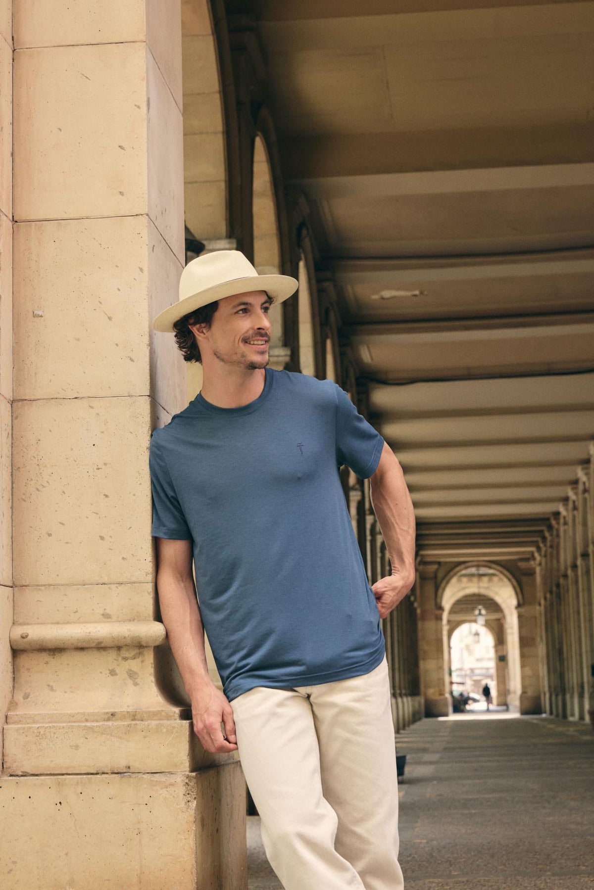 Man wearing a blue shirt and white hat standing in an architectural setting