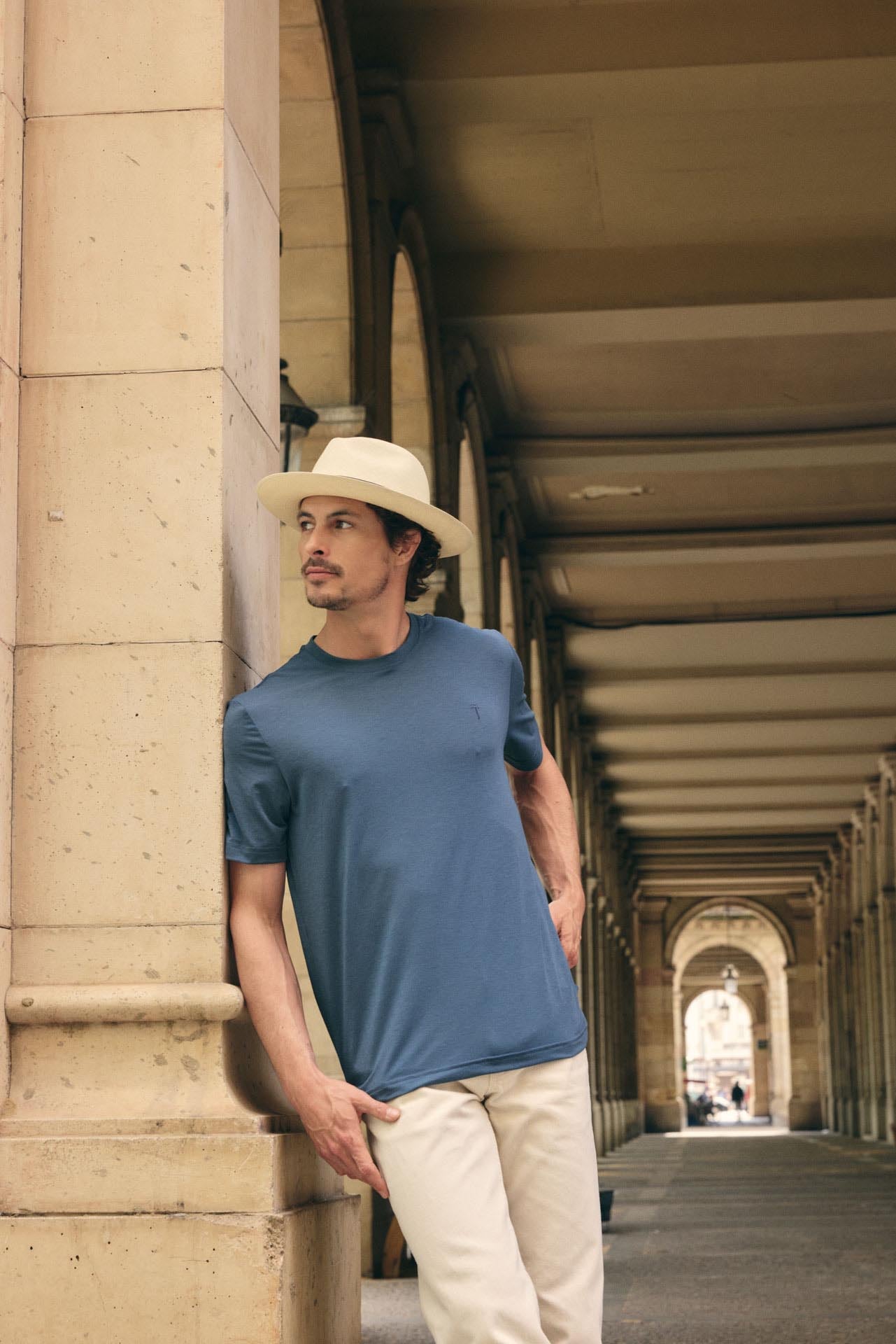 Man wearing a blue shirt and white hat standing in an architectural hallway