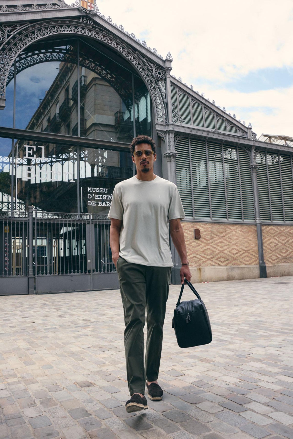 Man walking outdoors holding a black bag, with a building and glass facade in the background.
