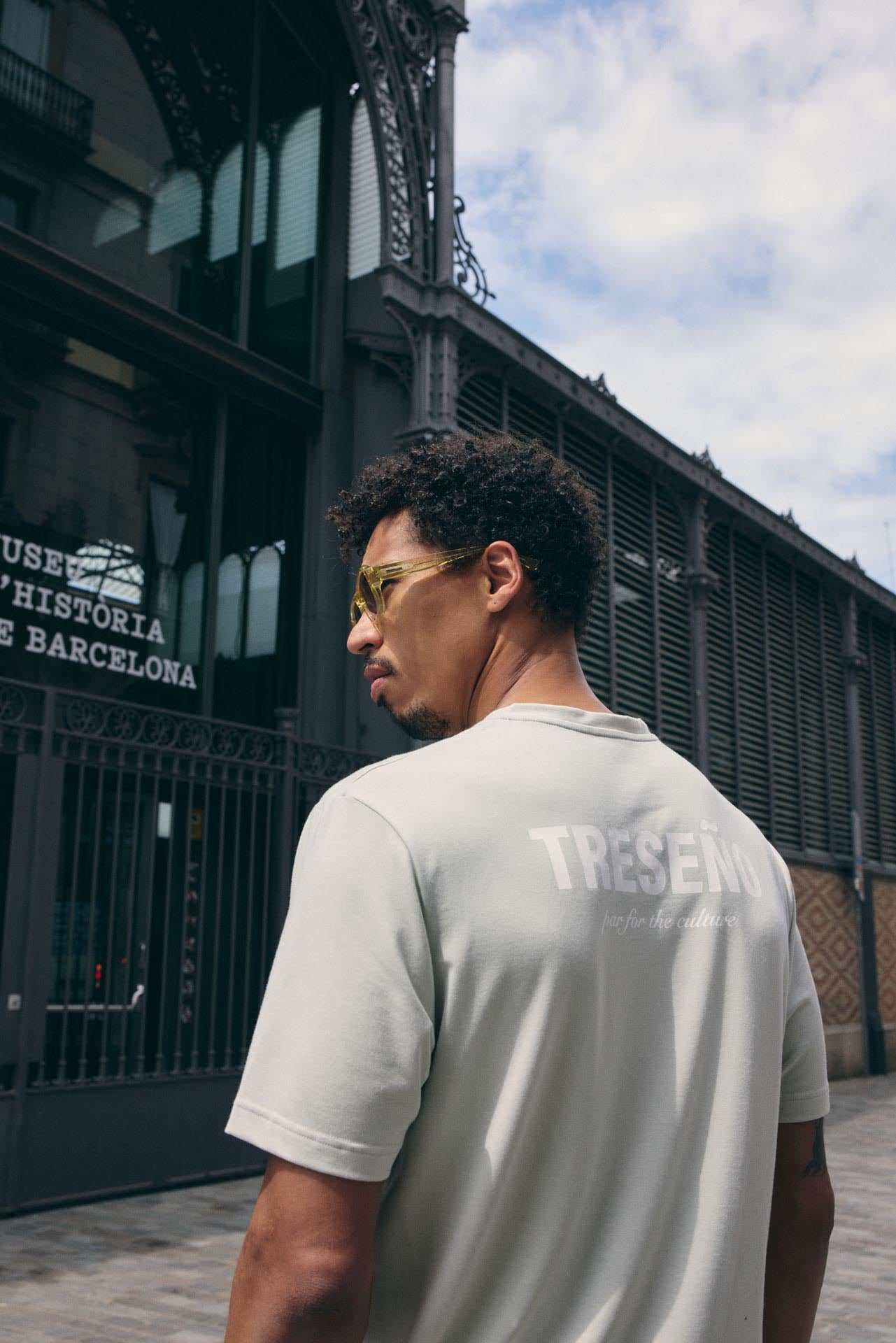 Man wearing a light gray t-shirt with 'TRESEÑO' branding, standing in front of a building with 'Museu d'Historia de Barcelona' sign.