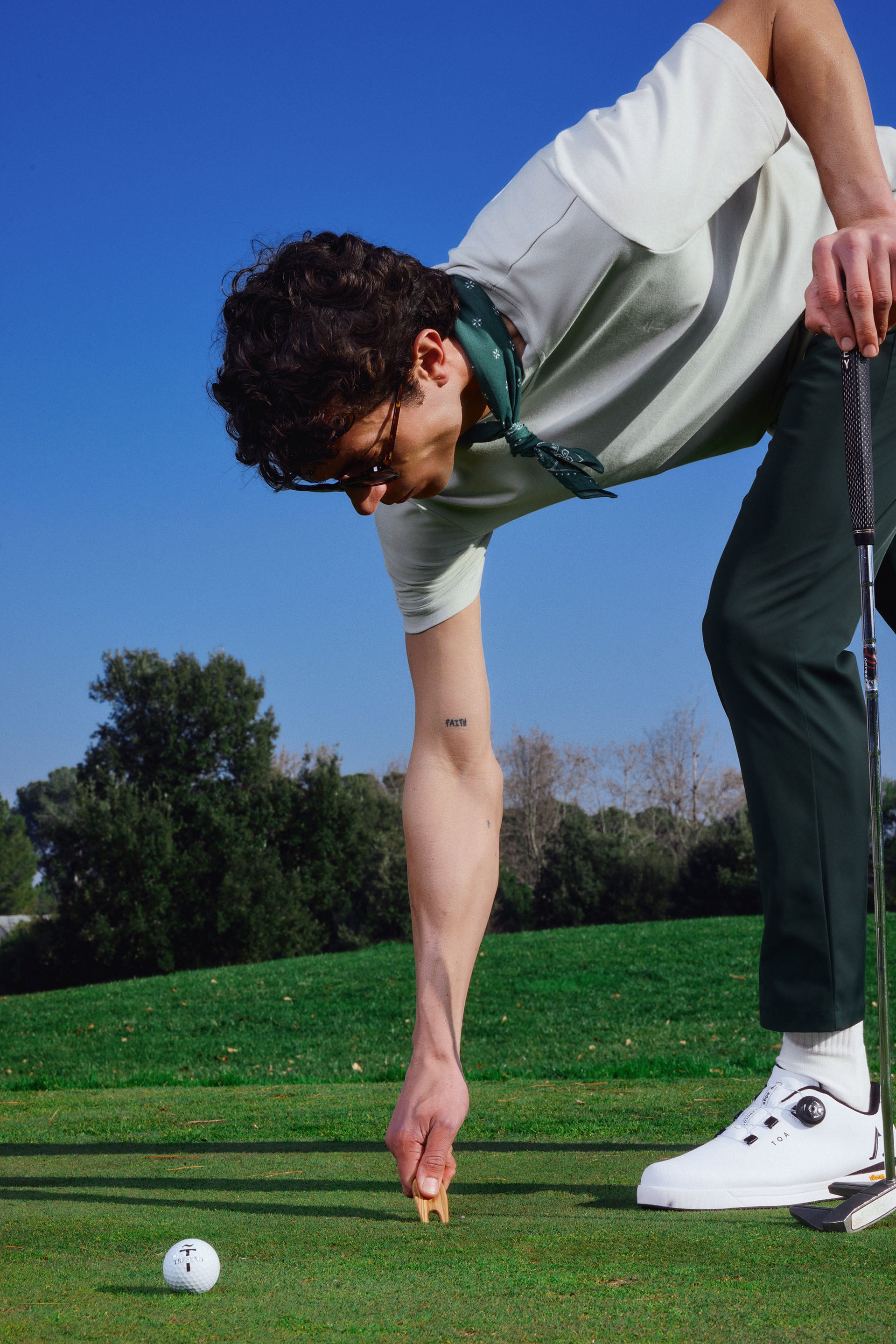 Person on a golf course fixing a ballmark with a clear blue sky and green grass in the background