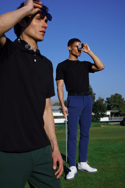 Two men on a golf course with one adjusting his sunglasses and the other holding a golf club.