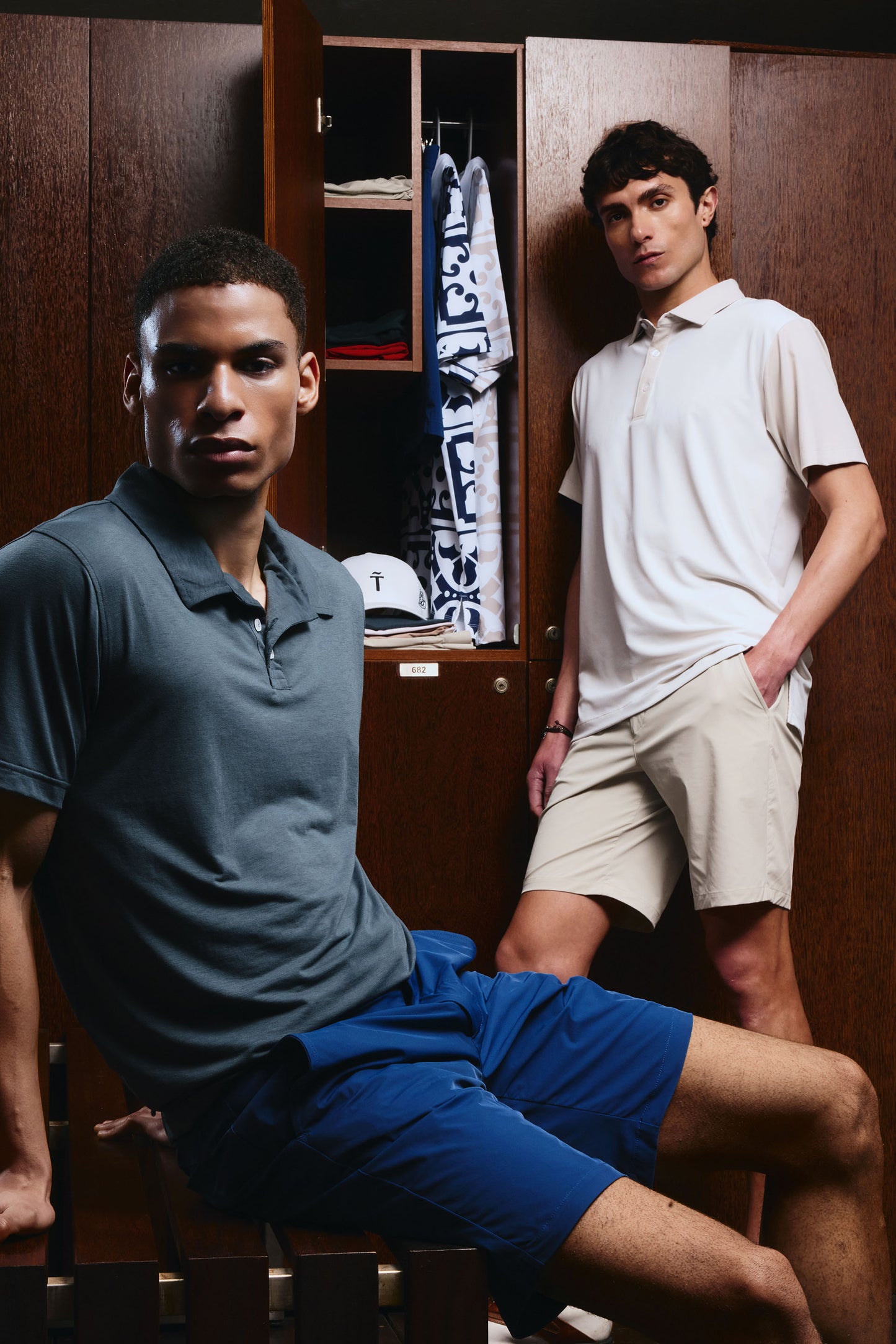 Two men in a locker room setting, one sitting and one standing.