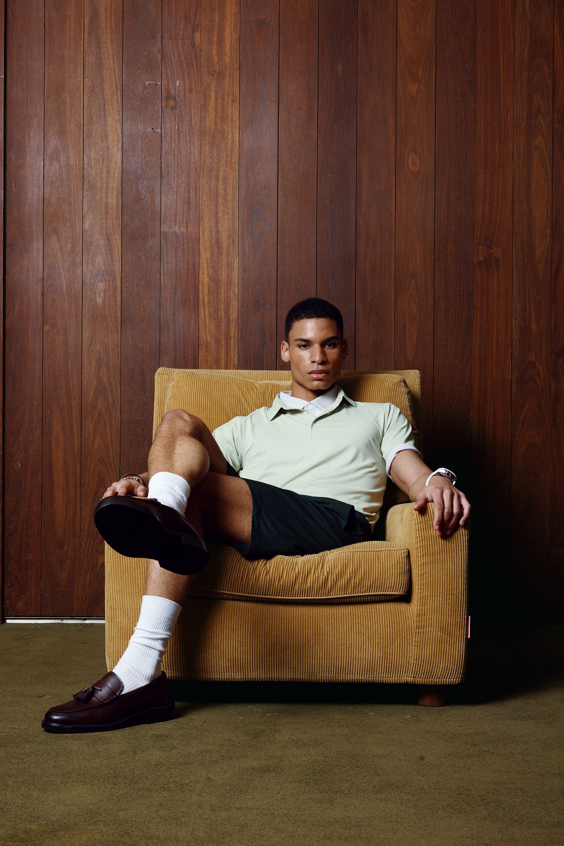 Man sitting in a brown armchair against a wooden paneled wall.
