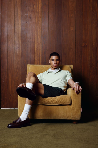 Man sitting in a brown armchair against a wooden paneled wall.