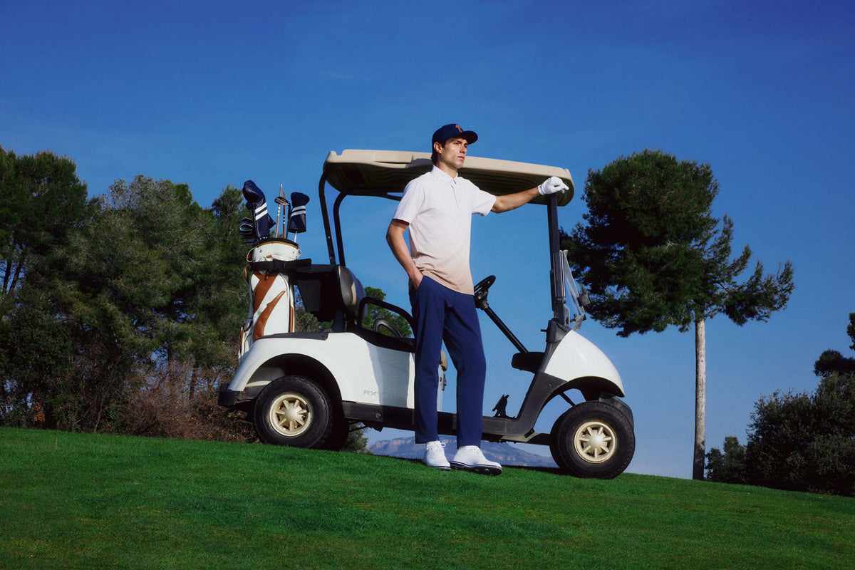 Man standing next to a golf cart on a golf course with trees in the background