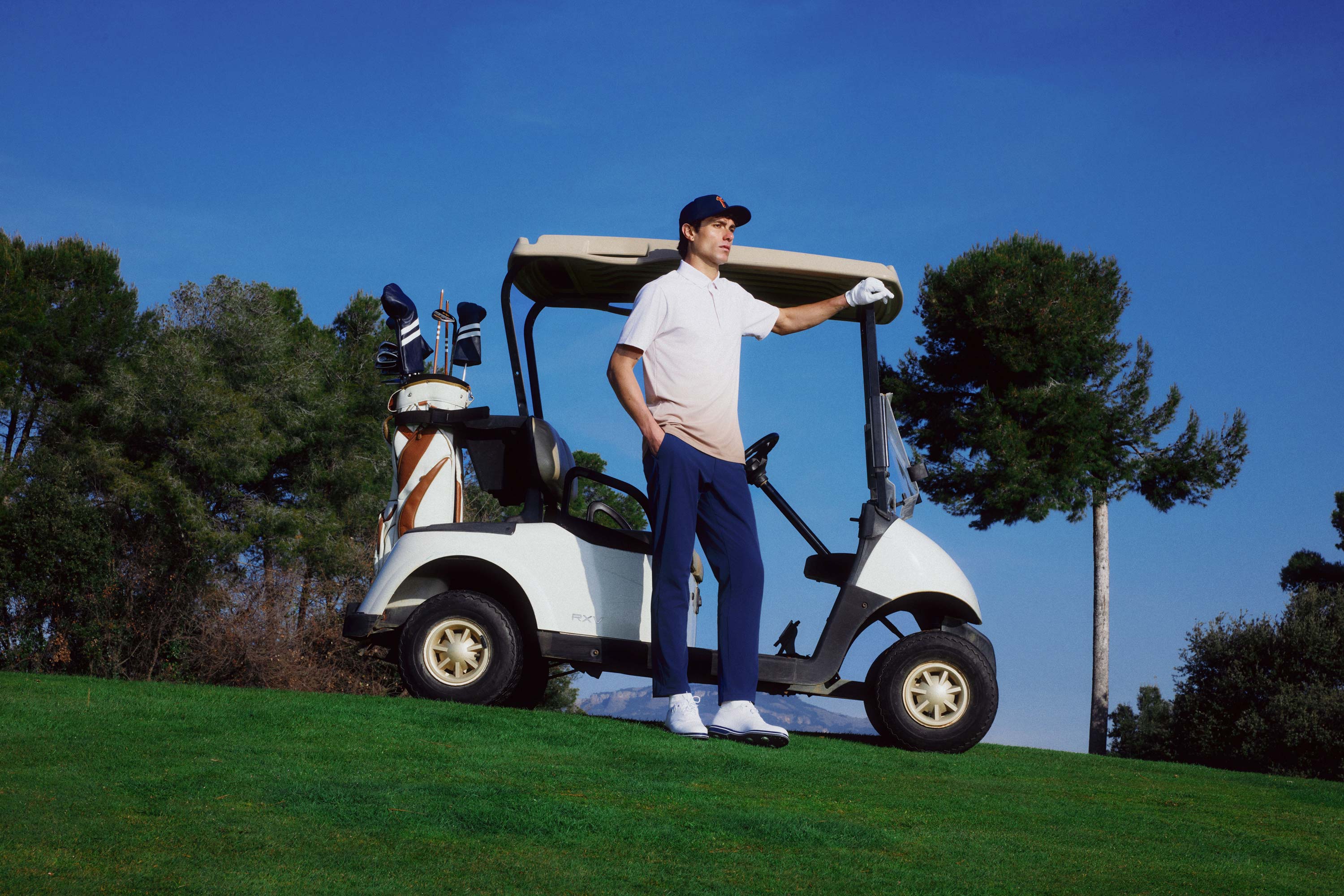 Man standing next to a golf cart on a golf course with trees in the background