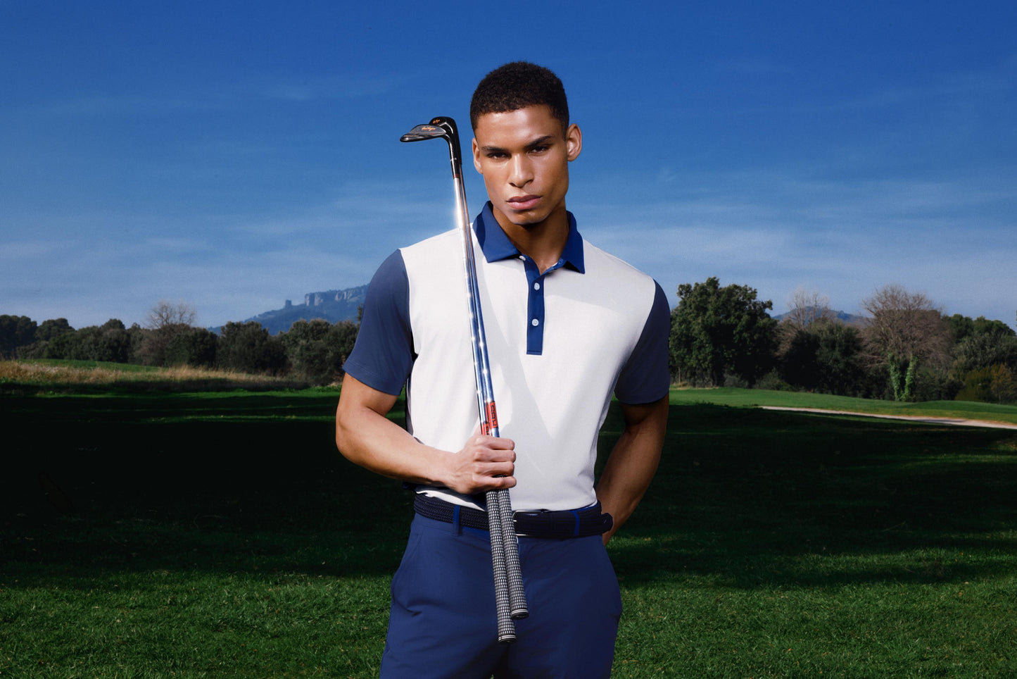 Man holding a golf club on a golf course with a clear blue sky