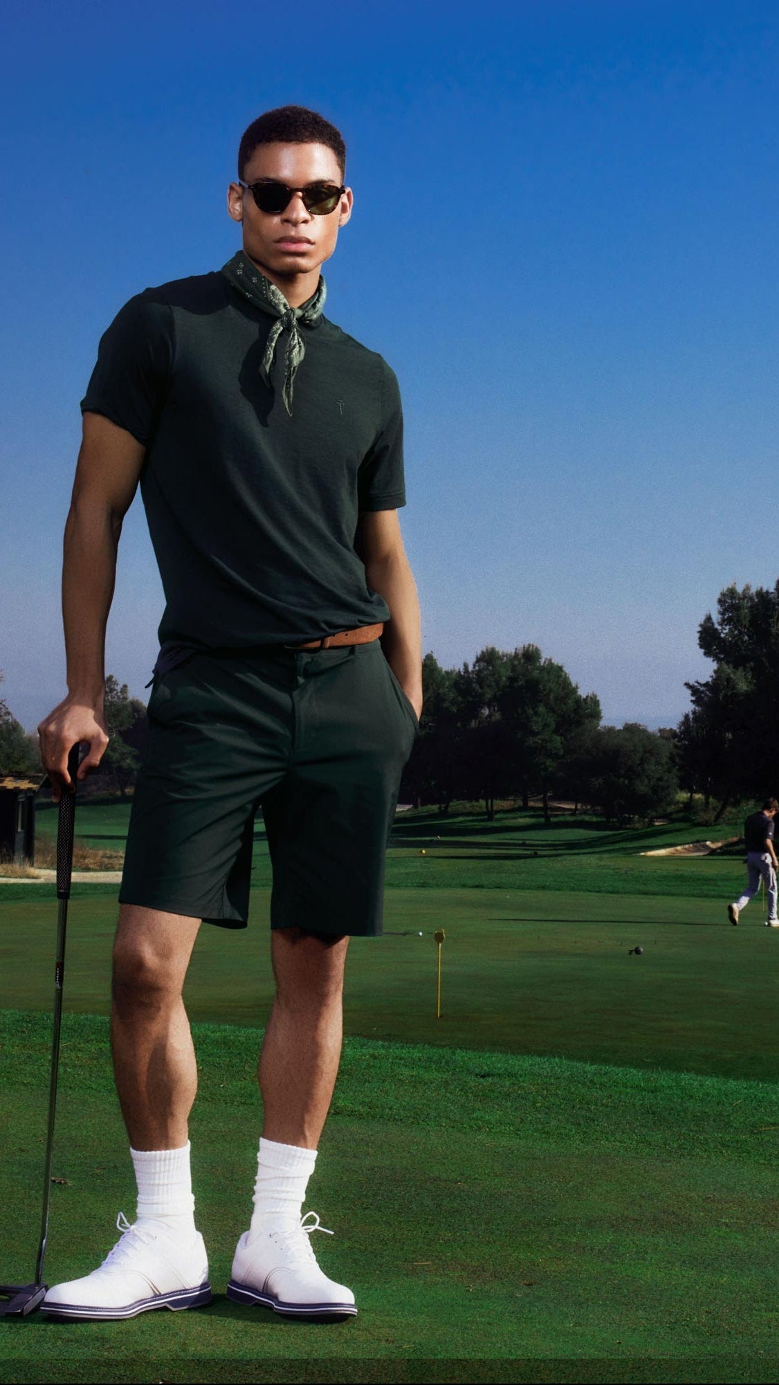 Man in golf attire standing on a golf course with a clear blue sky.