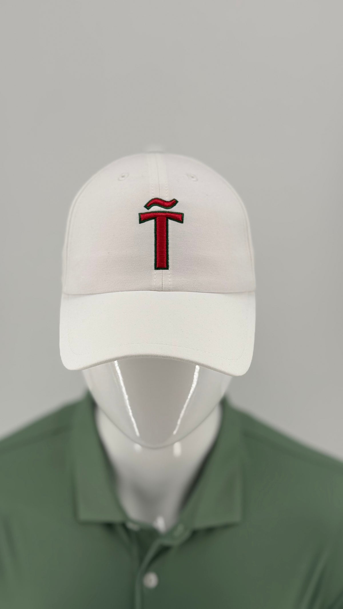 A white baseball cap with a red embroidered stylized 'T' logo on the front, displayed on a white mannequin head wearing a green polo shirt against a light gray background.