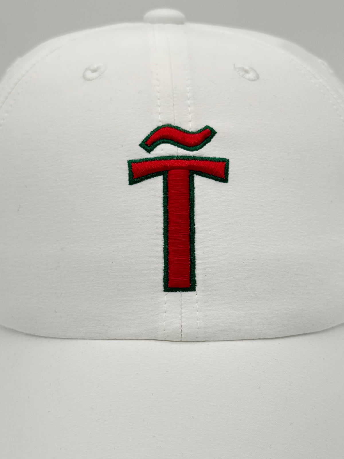 A white structured baseball cap featuring a prominent red embroidered letter 'T' with a green outline on the front panel.