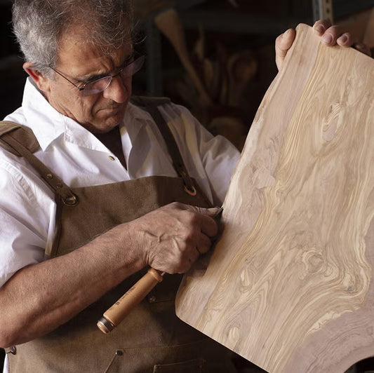 Man in a workshop using a tool on a olive wood plank